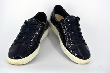 Stylish bright black lacquer shoes located on a white background. Moccasins made of genuine leather with bullshit and black wide laces. Women's sneakers on a white tast sole. 