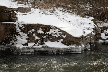 Amazing crystal icicle shapes hanging from the edge of snow covered riverbank during winter
