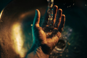a hand of person under a stream of water in a green and yellow light