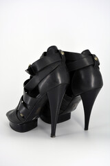 Black sandals on a thin high heel arranged on a white background. Stylish women's shoes made of genuine leather. Evening sandals with beautiful golden insole and twisted leather ribbon.