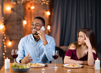 Black guy speaking on cellphone during dull date, his girlfriend feeling bored