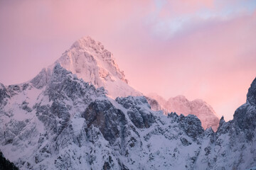Beautiful close up shot of a pink glowing Mountain top in the Alps at sunset while wind is blowing snow off the Mountain. Power of natural elements in an alpine environment