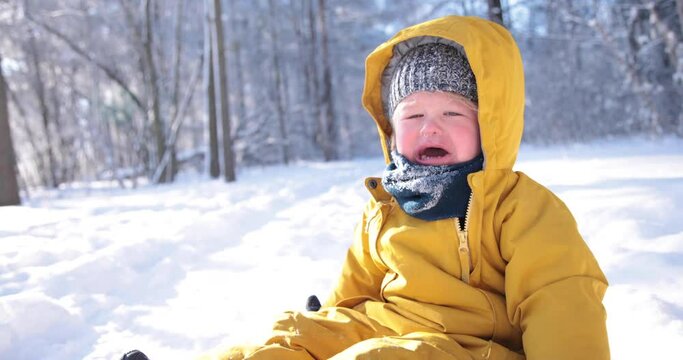 A young child crying because he has to play in the snow during a winter day