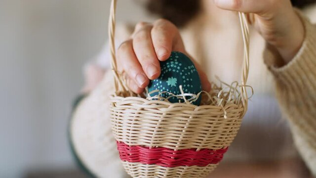 Close up of girl putting hand-painted Easter egg in a basket during egg hunting. Beautiful traditional decorated egg. Celebration of a happy Easter holiday, tradition and springtime. Slow-motion, 4K.