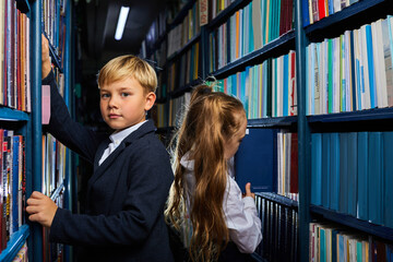 school children in library choosing books standing between shelves back to each other, preparing for school