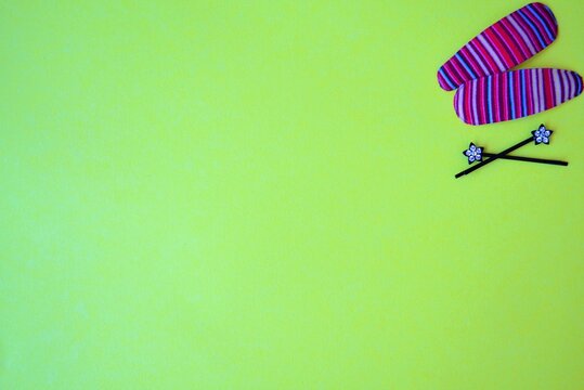 Two pink hair clips with strippe pattern in one corner on yellow background