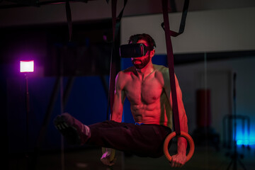 Fototapeta na wymiar Calisthenics athlete trains at gym rings with virtual 3d glasses.