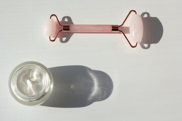 Concept of minimalistic skincare routine. Flat lay with moisturizer and rose quartz roller with contrasting shadows.