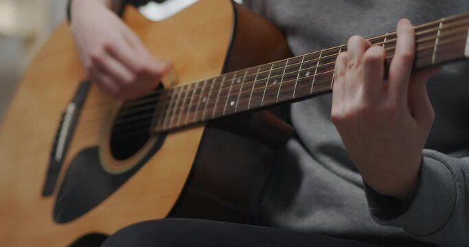A teenager learns new acoustic guitar chords at home after school. Close-up shot.