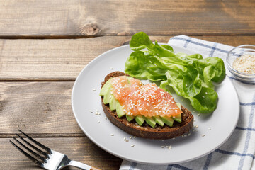 Whole grain rye bread toast with salmon and avocado on wooden table background. Close up, copy space