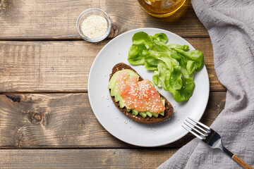 Whole grain rye bread toast with salmon and avocado on wooden table background. Flat lay, top view, copy space