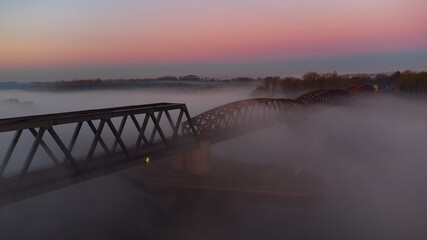 Obraz premium Bridge at Sunrise with a red sky in the Horizon . The picture was taken by a drone. the River unter the Bridge called Rhein. scary fog is around the bridge.