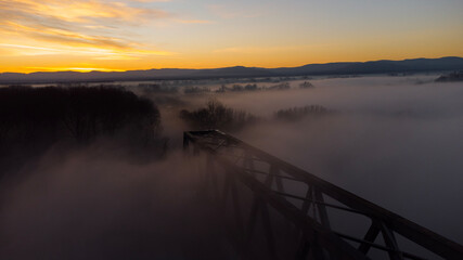 Bridge at Sunrise with a orange sky in the Horizon . The picture was taken by a drone. the River unter the Bridge called Rhein.  scary fog is around the bridge.