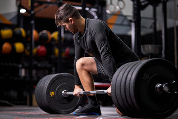 Fototapeta na wymiar Athlete standing on his knee preparing to make deadlift at gym, young caucasian man in black sportswear engaged in bodybuilding, concentrated on weightlifting. sport, cross fit