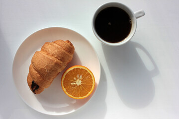 Cup of coffee, croissant and orange on white background. Top view, copy space. Morning espresso on table. Healthy breakfast. Direct light, hard shadow. 
