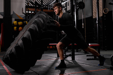 sportsman turns the tire, cross fit functional sport at gym. guy exercising with wheel sports, engaged in cross fit. sport concept