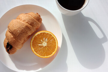 Cup of coffee, croissant and orange on white background. Top view, copy space. Morning espresso on table. Healthy breakfast. Direct light, hard shadow. 