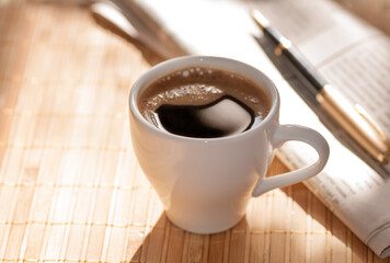 Cup of black coffee, newspaper and a pen on the table in the morning