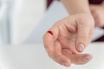 close up image of female hand with blood drop. Would due to cutting accident. Сareless handling of sharp objects.