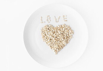 Heart of oatmeal on a white plate on a white background. Inscription Love from flakes. Space for text. 