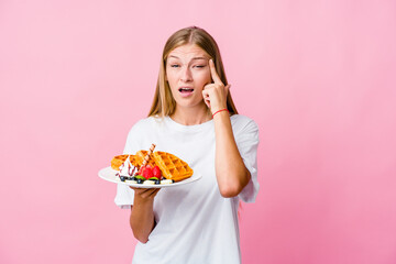 Young russian woman eating a waffle isolated showing a disappointment gesture with forefinger.