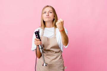 Young russian cook woman holding an electric mixer isolated showing fist to camera, aggressive facial expression.