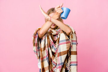 Young russian woman wrapped in a blanket drinking coffee keeping two arms crossed, denial concept.