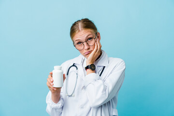 Young russian doctor woman holding pills bottle on blue who is bored, fatigued and need a relax day.