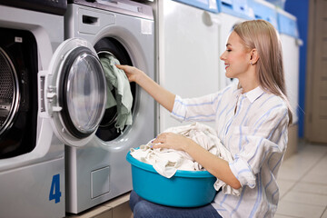 Housework: young woman doing laundry - putting white garments into the washing machine, in washng house, alone