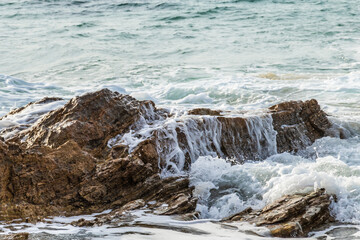 closeup of wave gently flowing over rock on california coastline; water cascading down the side. Pacific ocean in the background. 
