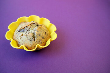 with a yellow silicone mold is a muffin with cherries, small pieces of dark chocolate, rice flour, corn flour, eggs and yogurt on a lilac background side view . homemade muffins