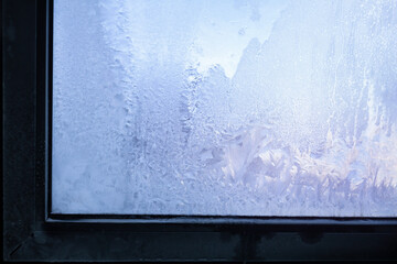 Blue frosty pattern on window glass with frame, winter background