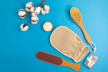 Natural wooden home accessories for foot and body peeling, dead sea salt and handmade cosmetic soap with white clay and charcoal on a blue background, top view, place for text. Plastic free life.