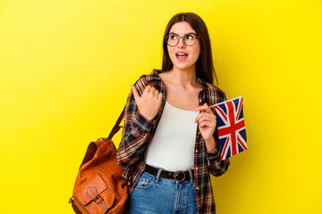 Young woman studying English isolated on pink background points with thumb finger away, laughing and carefree.