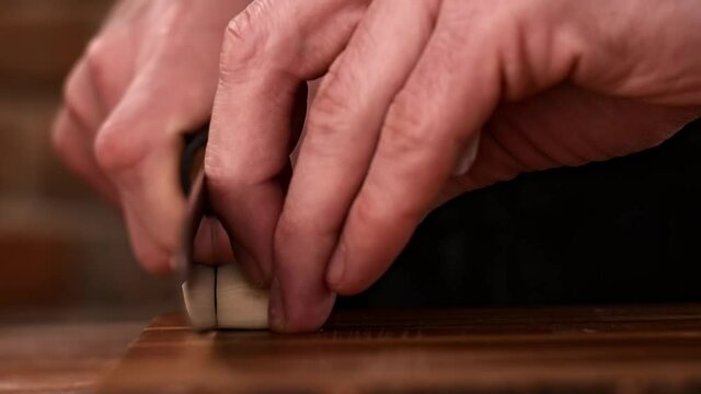 Cutting garlic into small slices with a knife on a wooden board
