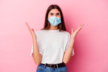 Young caucasian woman wearing a mask for virus isolated on pink background celebrating a victory or success, he is surprised and shocked.