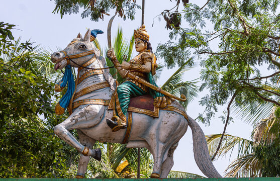 Chitradurga, Karnataka, India - November 10, 2013: Independence hero, Kittur Chennamma statue as woman with sword on horse in town with light blue sky and green foliage.