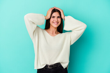 Young caucasian woman isolated on blue background laughs joyfully keeping hands on head. Happiness concept.