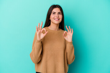 Young caucasian woman isolated on blue background cheerful and confident showing ok gesture.
