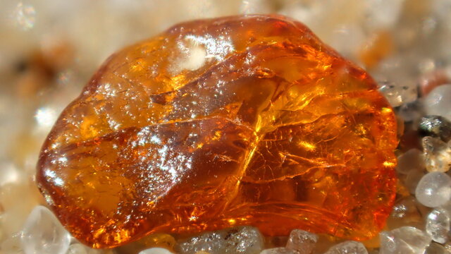 Close-up of a raw amber gemstone on sand, glowing with rich orange tones. Perfect for themes of nature, minerals, geology, or natural beauty