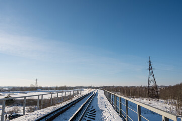 Snow-covered railway tracks and bridge. Winter landscape.  Sunny day. Blue sky. High voltage power line.