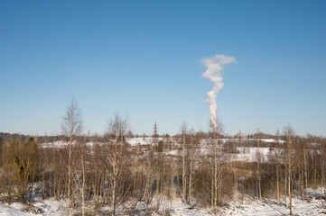 Winter landscape.  Sunny day. Blue sky. High voltage power line. White smoke. Naked trees. Forest.