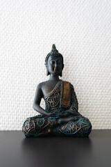 Buddha statue inside house in front of a white wall.