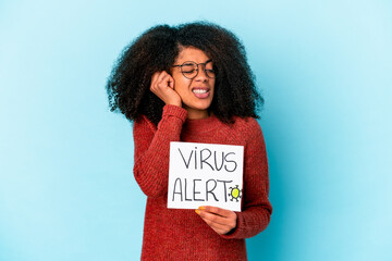 Young african american curly woman holding a virus alert placard covering ears with hands.