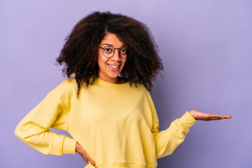 Young african american curly woman isolated on purple background showing a copy space on a palm and holding another hand on waist.