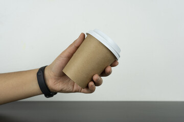 A hand grabs the take-away paper cup on a dark wooden table.