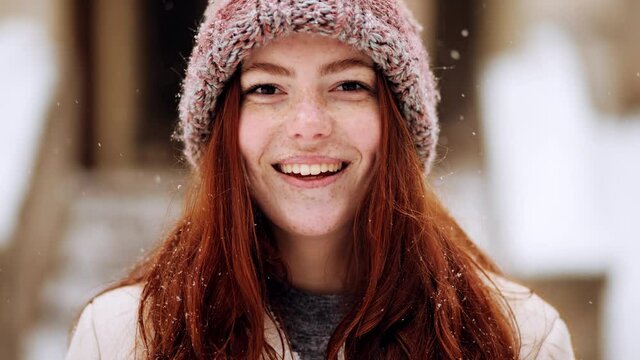 Close up portrait of smiling girl in snowy holiday city. Red haired woman with natural beauty and freckles on her face. Snowing outdoors. Winter concept