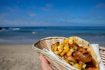 A hand holding a fish taco in basket in front of an ocean landscape in Mexico