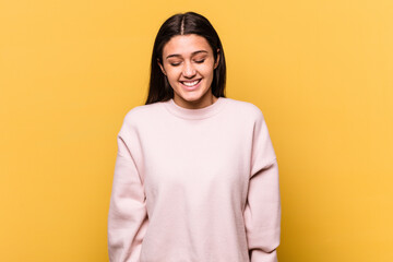 Young Indian woman isolated on yellow background laughs and closes eyes, feels relaxed and happy.