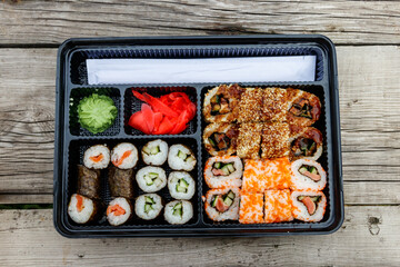 Set of sushi rolls in plastic box on wooden table. Sushi for take away or delivery of sushi in plastic container. Top view